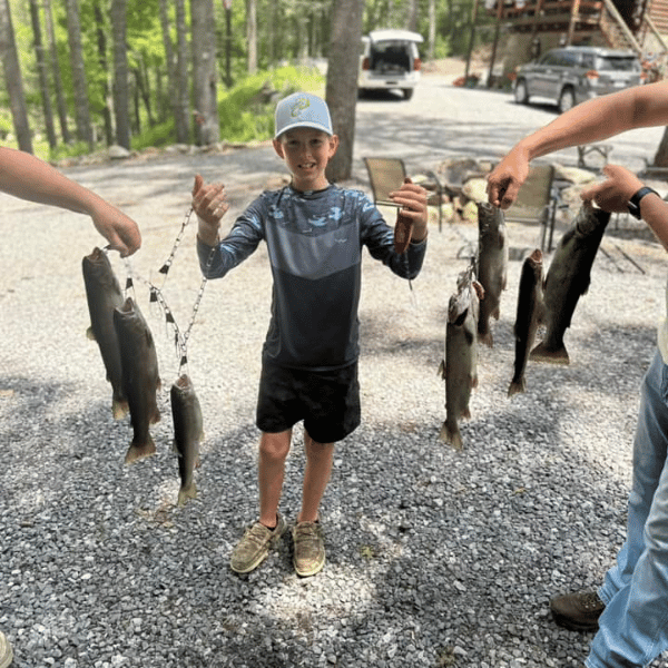 Young boy in blue grey HELIOS sun shirt displaying caught fish with family outdoors