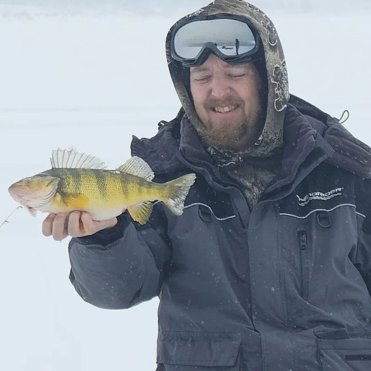 Angler in Boreas cold weather fishing gear on Alaska frozen lake with rainbow trout catch, demonstrating remote Bristol Bay ice fishing