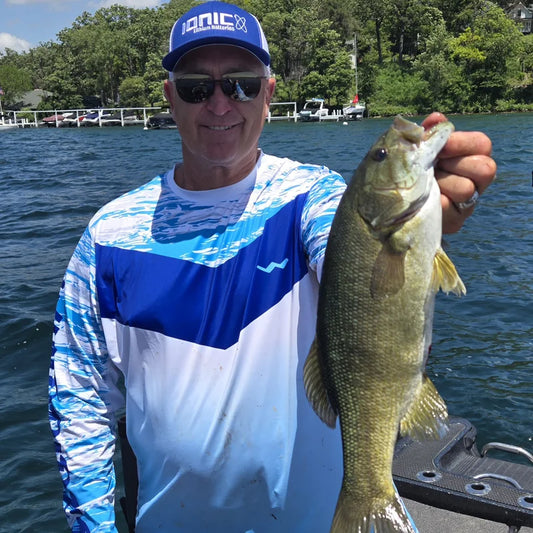 Angler wearing Helios long-sleeve performance fishing shirt on boat with bass catch in bright sunny conditions, demonstrating superior UPF 50+ sun protection and professional fishing performance