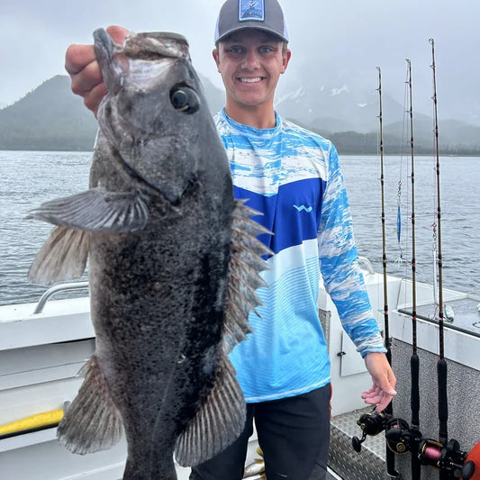 Fisherman in Helios long-sleeve UPF shirt on boat during midday sun displaying catch, demonstrating maximum sun protection during peak UV hours