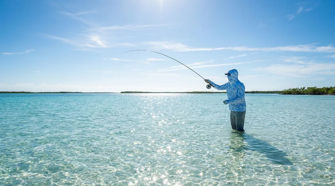 angler wading Bahamas flats in shallow turquoise water, bright tropical sun overhead, white sand bottom visible, holding fly rod and scanning for bonefish
