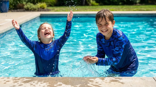 two kids around ages 5 and 8 playing in shallow pool water wearing long-sleeve UPF rash-guard-style sun shirts, bright midday sun, splashing and laughing