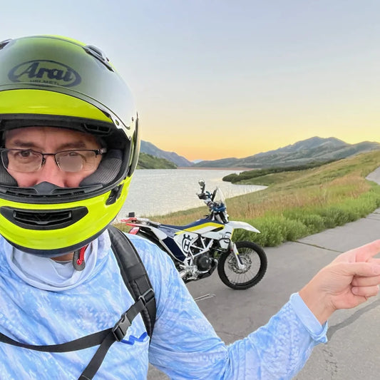Person wearing WindRider Helios hooded UPF sun shirt with helmet on scenic mountain road — demonstrating versatile sun protection for cycling and outdoor sports