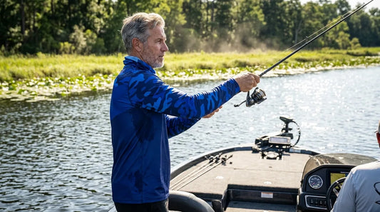 angler standing at the bow of a bass boat at midday, harsh overhead sun, water glare bouncing off the lake surface, casting toward a grassy bank in a tournament setting