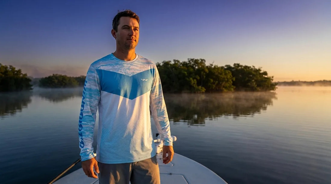 angler on the bow of a flats boat in early morning light, wearing a long-sleeve UPF fishing shirt, calm water and mangroves in background