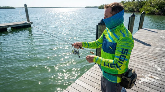 angler casting from a wooden dock over calm inshore water, midday sun overhead, wearing a long-sleeve UPF fishing shirt and neck gaiter pulled up, water sparkling with UV reflection