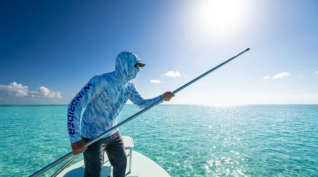 angler standing on the bow of a shallow-water skiff, poling over bright white sand flats, intense midday sun directly overhead, aqua water, light glaring off the surface
