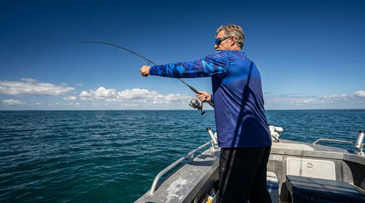 large-framed angler in long sleeve fishing shirt standing on a boat deck, midday sun overhead, casting with full arm extension showing sleeve coverage to the wrist
