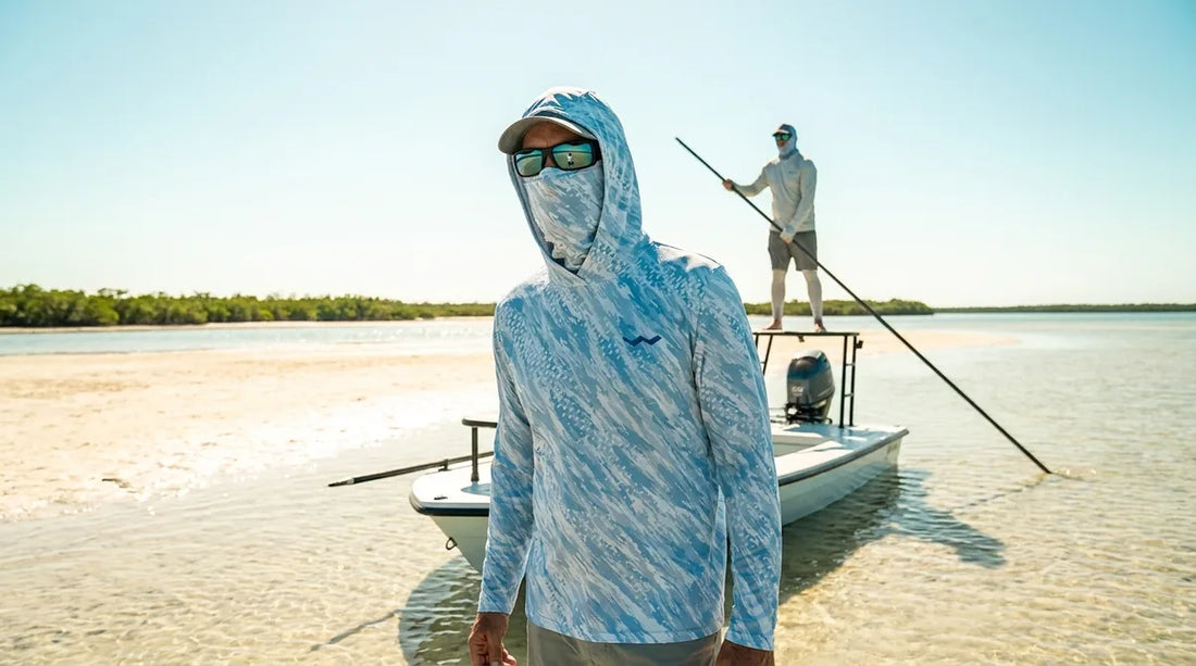 angler standing on the bow platform of a poling skiff on skinny water, hooded sun shirt with gaiter pulled up over nose and mouth, poling pole angler visible behind on platform, harsh midday light reflecting off pale sand flats