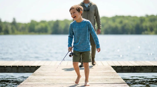 a kid around age 8 wearing a long-sleeve sun shirt on a lake dock, mid-laugh, holding a small fishing rod, parent visible nearby out of focus, bright midday light