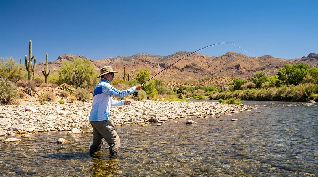 fly fisherman wading the Salt River in Arizona, bright summer midday sun, low desert mountains in background, clear shallow water, angler in long-sleeve UPF shirt casting a fly rod