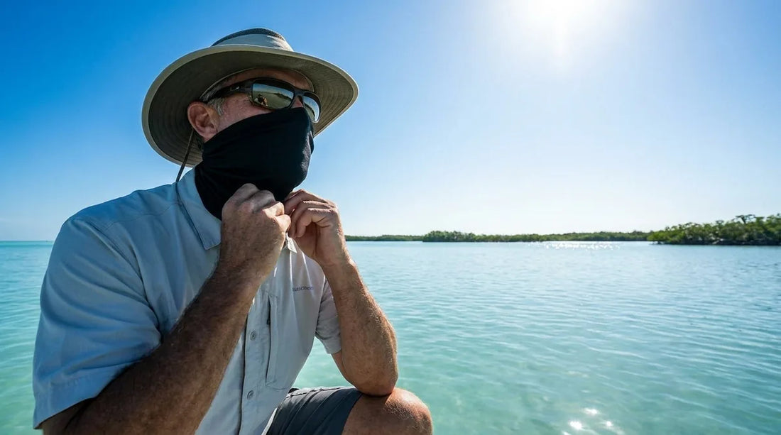 angler on a saltwater flat adjusting a neck gaiter pulled up over nose and chin, bright midday sun, calm blue water in background