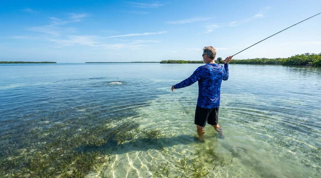 angler wading a shallow Gulf Coast grass flat, knee-deep water, bright morning sun, casting to a seatrout school in the distance, wearing a light-colored long sleeve UPF fishing shirt
