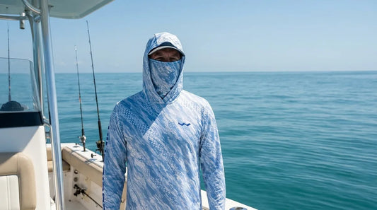 angler on a center console in full sun offshore, wearing a hooded UPF fishing shirt with integrated gaiter pulled up, calm blue-green water behind, midday light harsh and direct