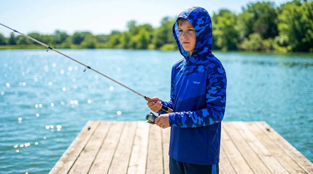 young angler around age 10-12 wearing a hooded UPF fishing shirt, standing on a dock with rod in hand, bright summer sun overhead, water visible in background