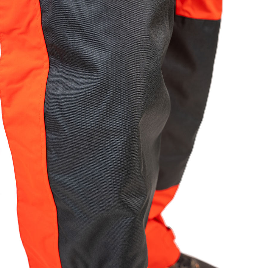 Close-up of a red WindRider rain bib leg showing the heavier-weave charcoal reinforcement panel sewn over the knee