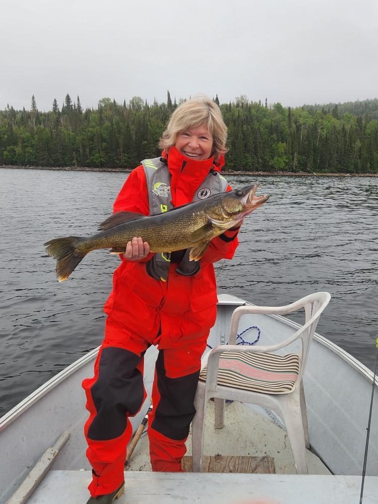 Customer holding a walleye on a northern lake wearing the red Pro All-Weather suit with black shoulder panels
