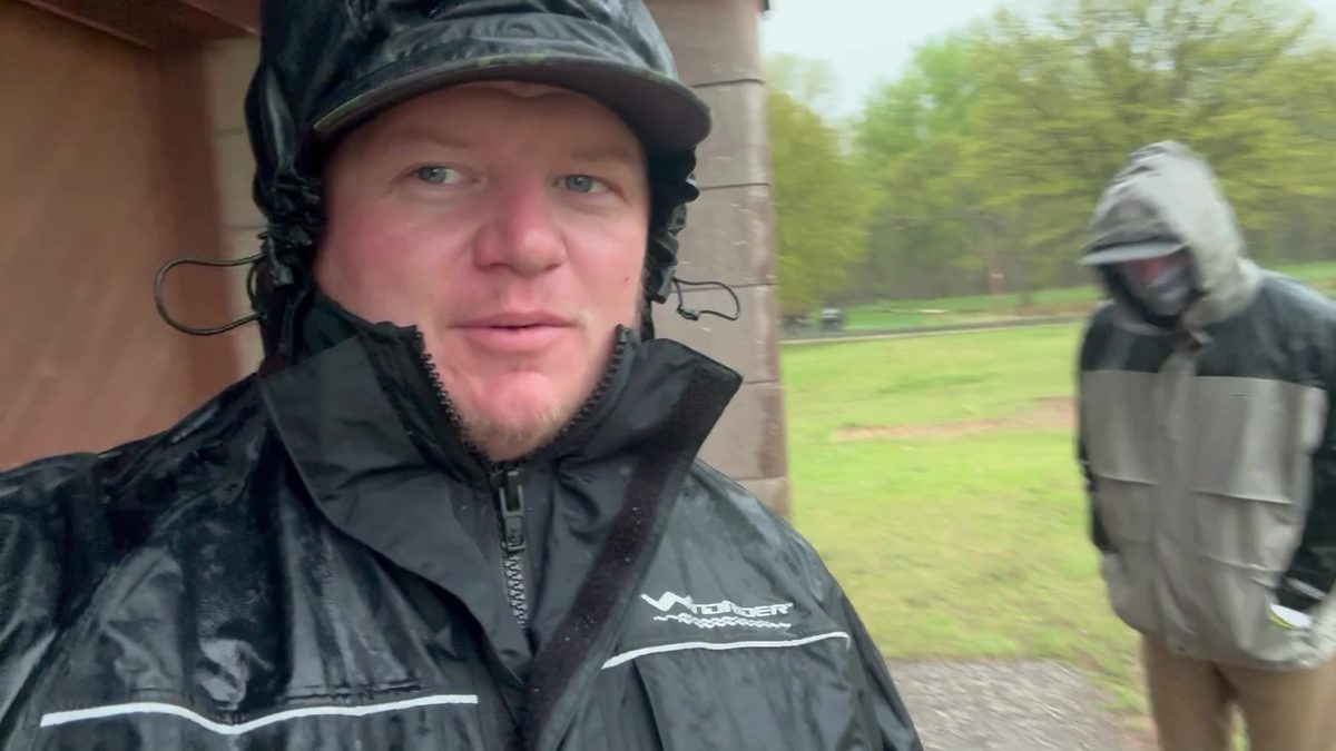 Customer in the black Pro All-Weather jacket, hood cinched down, standing in heavy rain